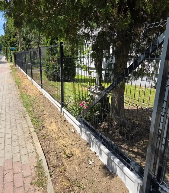 Ogrodzenie panelowe w kolorze grafitowym na gładkiej podmurówce wzdłuż chodnika