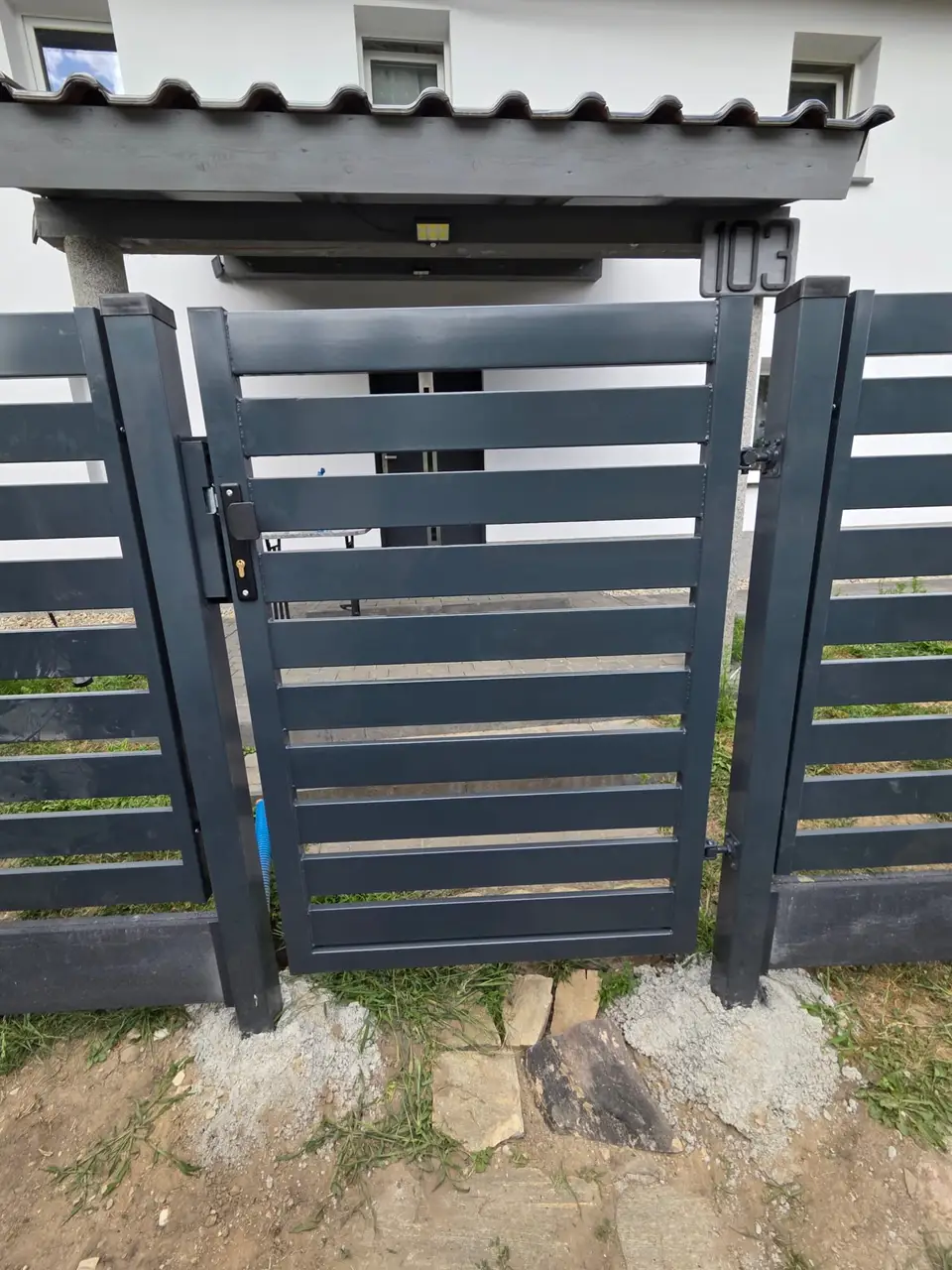 Furtka palisadowa w kolorze grafitowym między słupkami ogrodzenia